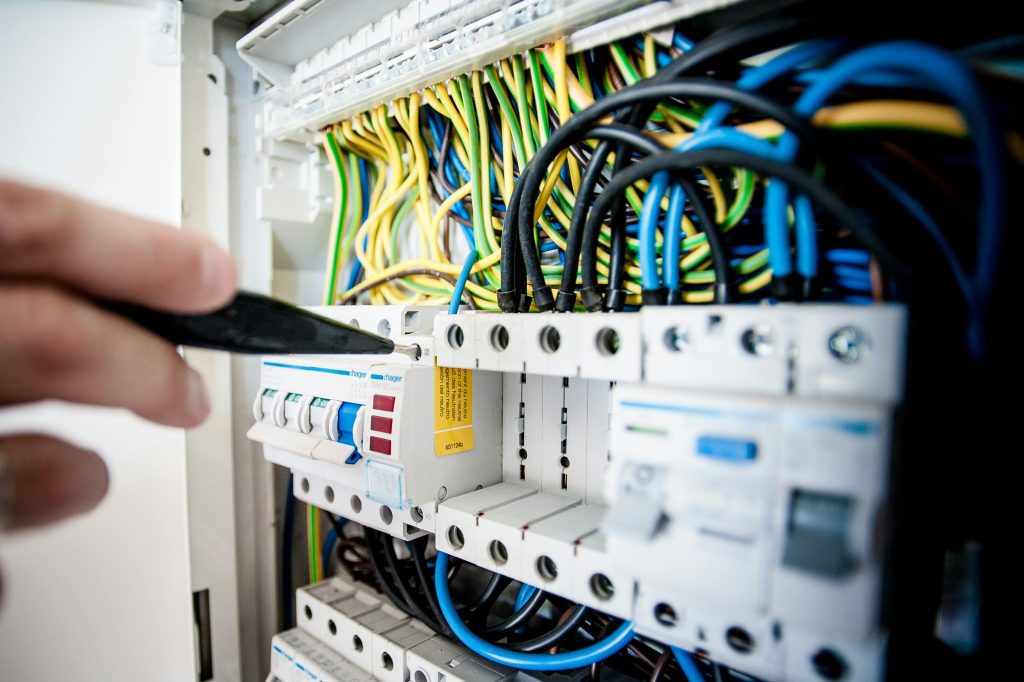 Electricista-Zaragoza Hand of electrician working on a circuit breaker panel with colorful wires, ensuring safe electrical connections. reformas integrales en Zaragoza
