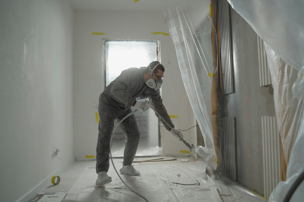 pexels-photo-6474300-6474300 A worker in protective gear painting walls during an indoor renovation project.